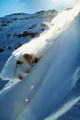 Man skiing off piste with pole out stretched for the turn with a snow rooster by him, caught in the sun. Ross Woodhall - Action & Lifestyle Photography