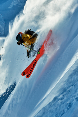 Man skiing off piste with ski crossed over on a steep slope with snow particles behind him. Ross Woodhall - Action & Lifestyle Photography