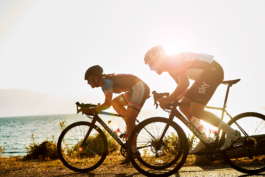 two cyclist cycling along a road with the sea in the background. Ross Woodhall - Action & Lifestyle Photography