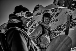 Skier and snowboarder resting after hiking. Image in black and white. Skier smiling towards the camera behind the snowboarder. Ross Woodhall - Action & Lifestyle Photography