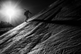 Skiing hiking up an off piste hill with ski's over his shoulder with backpack on with sun shinning. Image in black and white. Ross Woodhall - Action & Lifestyle Photography