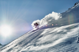 Solo skier off piste wearing backpack. Skiing downhill with sun shinning in the background with blooms of snow Ross Woodhall - Action & Lifestyle Photography