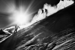 Black and white image of two skiers. skiing off piste with blooms of snow and the sun shinng towards the camera. Ross Woodhall - Action & Lifestyle Photography