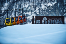 La Grave multi coloured telecabines with sign, with icy cold looking rock and pine trees in background. Le Meije. In the Massif des écrins range Ross Woodhall - Action & Lifestyle Photography