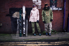 Two Skiers posing in Manchester side street fully kitted out leaning against a graffiti bricked wall. with skis and poles Ross Woodhall - Action & Lifestyle Photography