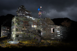 Man balancing on rear wheel of mountain bike on a old slate building wall. shot with flash with dark clouds in background. Ross Woodhall - Action & Lifestyle Photography