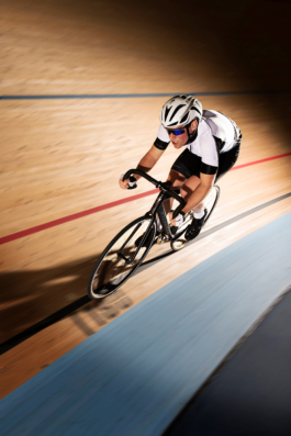 Man on bike cycling on velodrome circuit with flash to highlight him. Ross Woodhall - Action & Lifestyle Photography