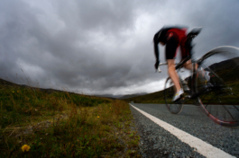 blurry image of a road biker on his bike on a country road by the grass verge. Ross Woodhall - Action & Lifestyle Photography