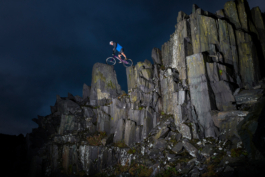 Man on a mountain bike balanced between two pieces of slate at a height, lit with a flash, taken at night. Ross Woodhall - Action & Lifestyle Photography