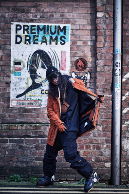 Man wearing full ski wear with open jacket in front of brick wall with poster behind. Ross Woodhall - Action & Lifestyle Photography