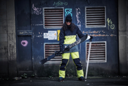 Man with pair of skis and poles wearing winter ski wear as streetwear in front of graffitied air vents. Ross Woodhall - Action & Lifestyle Photography