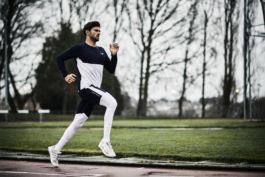 Man running along running track with grass and trees in background. Wearing Castore clothing. Ross Woodhall - Action & Lifestyle Photography