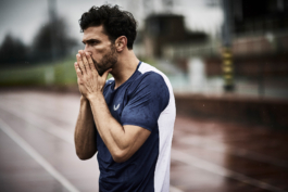 Man in the rain on running track, holding his hands up to his mouth. Castore branded clothes. Ross Woodhall - Action & Lifestyle Photography
