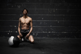 man shirtless, working out at gym with weighted gym ball. wearing Castore shorts. Ross Woodhall - Action & Lifestyle Photography