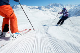two skiers going down a groomed slope, surrounded by mountains. Ross Woodhall - Action & Lifestyle Photography