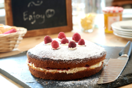 Afternoon cake, victoria sponge with cream and raspberries on a slate with a knife. Plates and jam in the background. Ross Woodhall - Action & Lifestyle Photography