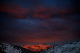 3 snowy mountains with the middle mountain covered in sunset colours & lighting. Heavy red/purple clouds. Ross Woodhall - Action & Lifestyle Photography