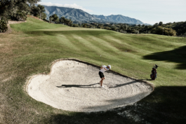 Man playing golf mid swing towards the green from a sand bunker. Ross Woodhall - Action & Lifestyle Photography