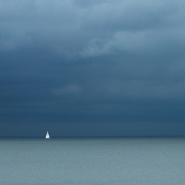 Looking out over a calm sea with dark clouds with a bright sailing boat with sails. Ross Woodhall - Action & Lifestyle Photography