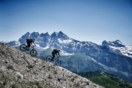 two mountain bikers going down a rocky mountain ridge in an Alpine setting, with snow tipped mountains in the back ground. Ross Woodhall - Action & Lifestyle Photography