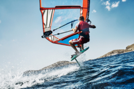 Rear view of windsurfer jumping out of the water with land in the background. Image taken from the water. Ross Woodhall - Action & Lifestyle Photography