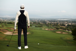 Man playing golf, looking down on the golf course, golf ball on a tee. Man wearing Castore clothing and a glove. Ross Woodhall - Action & Lifestyle Photography
