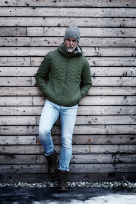 bearded middle aged man, wearing jacket and hat, stood in front of a wooden wall. Ross Woodhall - Action & Lifestyle Photography