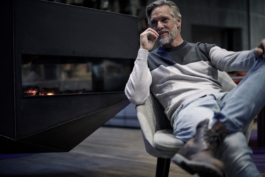 man with beard, sat casually with one knee up in front of a modern fire place. Ross Woodhall - Action & Lifestyle Photography