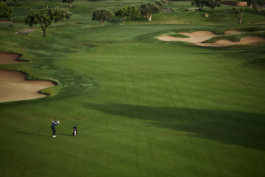 Image of a man playing golf, from a distance, mid swing before hitting the ball towards the green, with a sand bunker off to the right just before the green. Ross Woodhall - Action & Lifestyle Photography