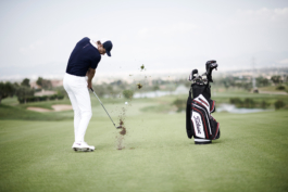 Man playing golf, wearing Castore clothing. Hitting the ball with turf flying up and golf bag beside him. Ross Woodhall - Action & Lifestyle Photography