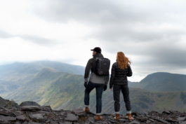 A man & woman out hiking, stood on a cliff edge looking out on to the view. Man is wearing a backpack with a cap. Woman has red hair blowing in the breeze both are wearing Land Rover, Musto branded clothing. Shoot for theur advertising campaign. Ross Woodhall - Action & Lifestyle Photography