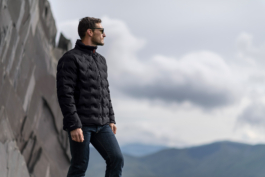 Man looking out into the distance against a rocky cliff side wearing a light weight black quilted jacket from Land Rover, Musto brand. Wearing sunglasses & jeans. Ross Woodhall - Action & Lifestyle Photography