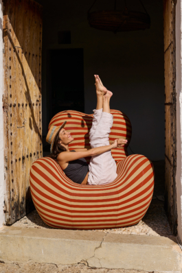 woman out stretching her legs upwards wearing a straw hat, on a stripy chair in an old large doorway. Ross Woodhall - Action & Lifestyle Photography