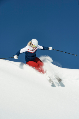 female skier carving in the snow with poles out stretched. Ross Woodhall - Action & Lifestyle Photography
