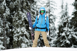 female skier, posing with skis in her hand in front of some trees. Ross Woodhall - Action & Lifestyle Photography