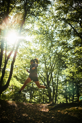 female runner jumping, mid air on a woodland path in the trees. Ross Woodhall - Action & Lifestyle Photography