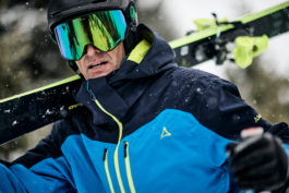 male skier, walking with skis over their shoulder, looking towards the camera. Ross Woodhall - Action & Lifestyle Photography