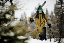 male skier walking with skis over their shoulder, between the trees. Ross Woodhall - Action & Lifestyle Photography