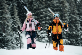 A couple of skiers walking with skis over their shoulders with trees in the background. Ross Woodhall - Action & Lifestyle Photography