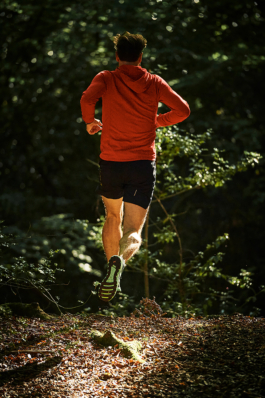 male jogger, wearing shorts, running away from the camera, caught mid air. surrounded by greenery. Ross Woodhall - Action & Lifestyle Photography