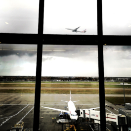 view from a window at an airport with British Airways planes, one just taken off and one with walkway connected. Ross Woodhall - Action & Lifestyle Photography