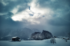 old small farm building covered in snow, with mountain in the background with moody clouds. Ross Woodhall - Action & Lifestyle Photography