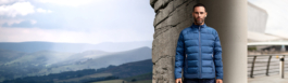 Split image of a man standing slightly off centre of the photo wearing a light blue quilted jacket by Land Rover brand. On his left is a city background & on his right is a view of some hills. Ross Woodhall - Action & Lifestyle Photography