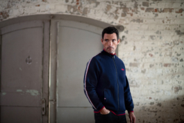 Man wearing a blue zip through cardigan with red & white trim down the sleeve with red Jaguar branding logo on left hand side of chest. Ross Woodhall - Action & Lifestyle Photography