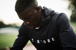 Black/ethnic/coloured man wearing a black waterproof hoody with beats of water on the hoodie, branded with Castore. Man has beats of sweat on his face. Ross Woodhall - Action & Lifestyle Photography