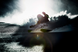Solo skier, coming downhill in deep snow with a snow rooster. In front of the sun so he is silhouetted, left pole high in the air. Ross Woodhall - Action & Lifestyle Photography