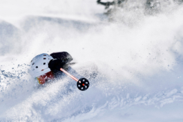 Solo skier in deep snow with left arm & left pole lifted high. Wearing a white helmet. Ross Woodhall - Action & Lifestyle Photography