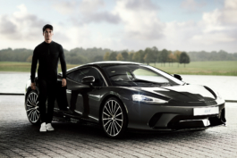 Man standing by a Mclaren GT sports car, wearing Mclaren Castore clothing in front of a lake at Mclaren home show room. Ross Woodhall - Action & Lifestyle Photography