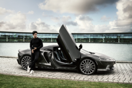 Man leaning against a Mclaren sports car with the door open, in front of the lake and home show room of Mclaren. Ross Woodhall - Action & Lifestyle Photography