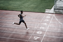 Black/ethnic/coloured man on running track coming up to finish line. He is looking at his watch. Running in lane 6. Wearing Castore branded clothing, a sleeveless t shirt and shorts with white trainers. Ross Woodhall - Action & Lifestyle Photography